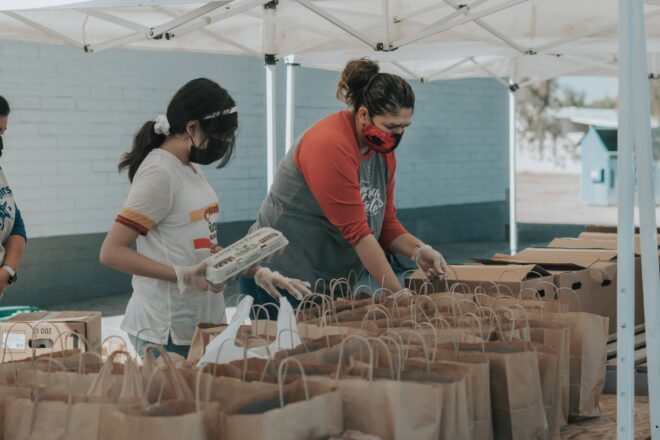 Mulheres fazem trabalho voluntário com distribuição de alimentos em sacolas